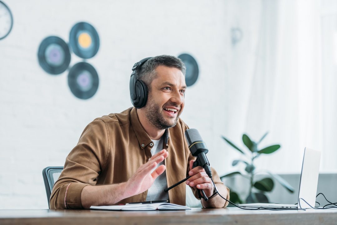 cheerful-radio-host-gesturing-while-recording-podcast-in-broadcasting-studio.jpg